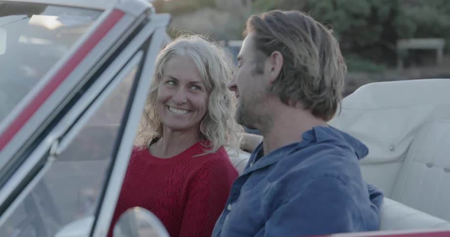 A man and woman smile and laugh inside a car