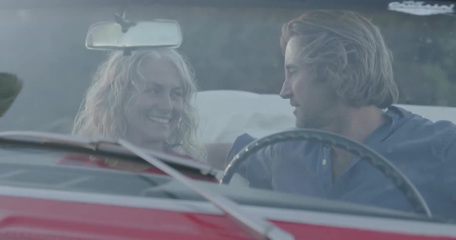 Man and woman sit in a red convertible car