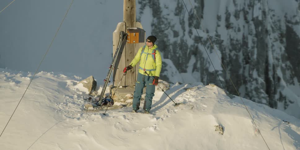 A man stands on the mountain near a wooden post