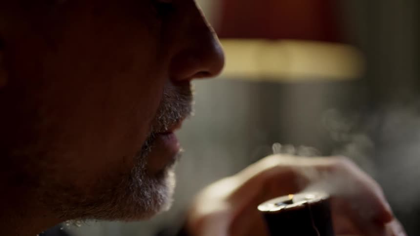 A man is blowing out a candle as he sits inside in daylight