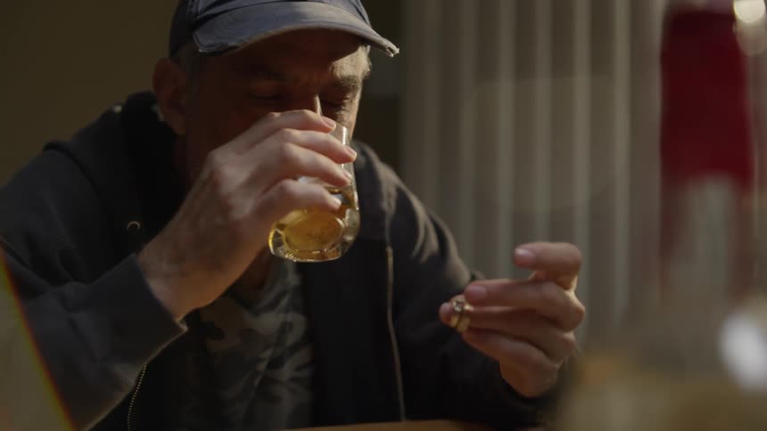 A man drinks whiskey while holding two wedding rings