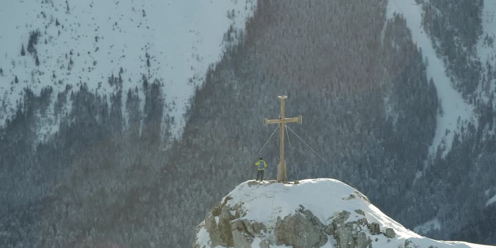 A skier stands on a peak next to a cross