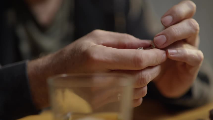 A man is sitting at a table holding two wedding rings in the daylight