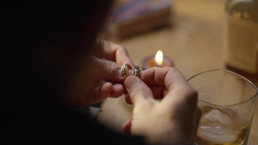 Man holds wedding rings while drinking whiskey