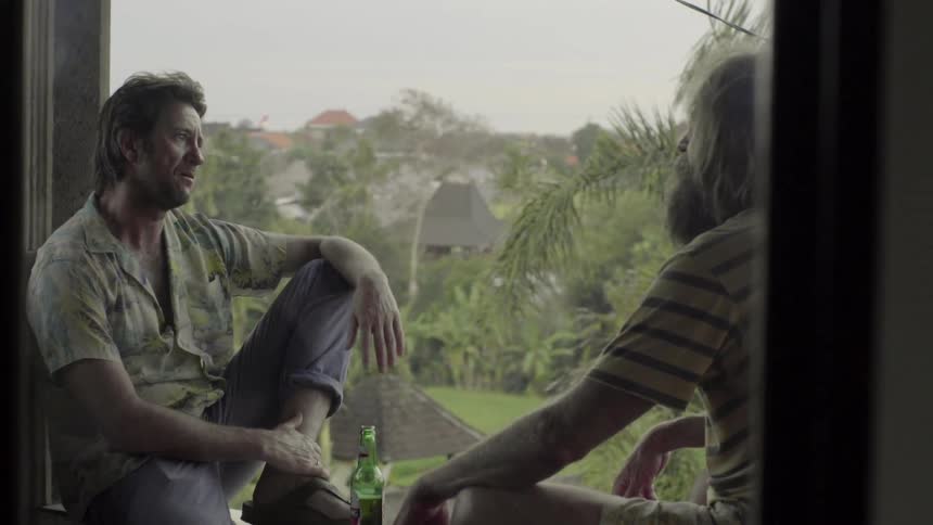 Men sit facing each other on a porch railing talking
