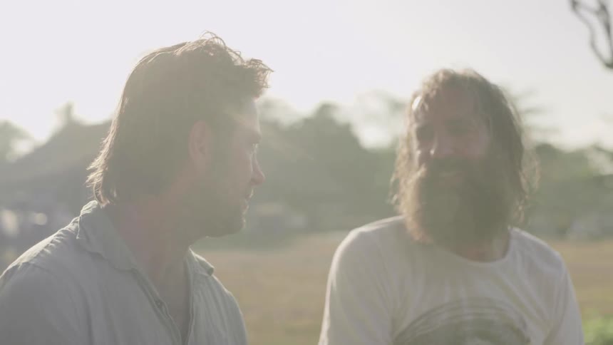 Two men sit outside talking on a sunny day