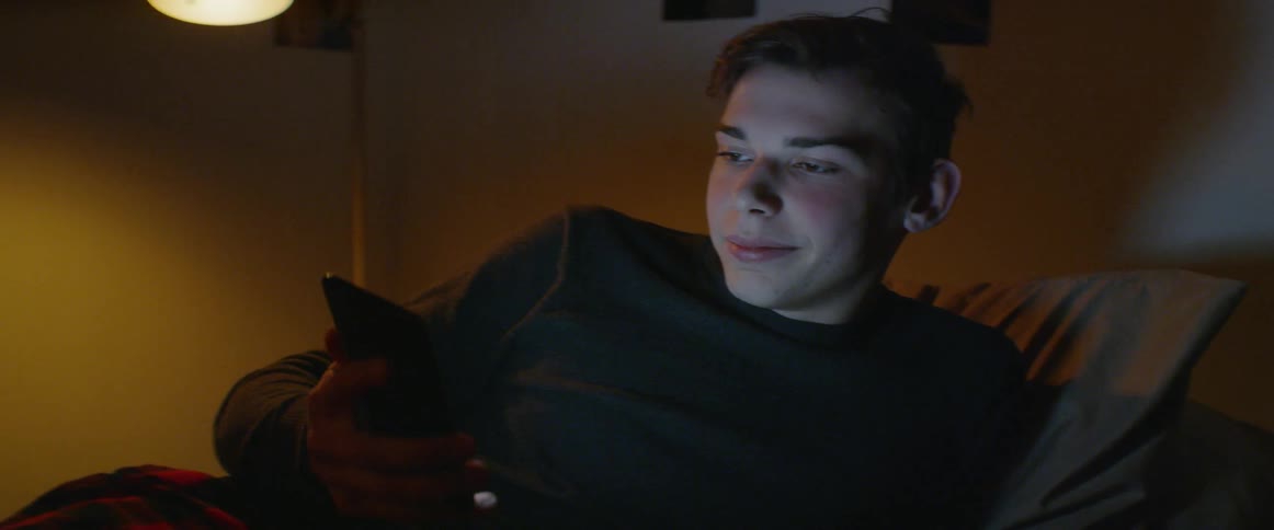 Teenager sits in bed smiling at his phone