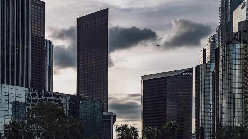 Clouds float over skyscrapers and the sun shines overhead