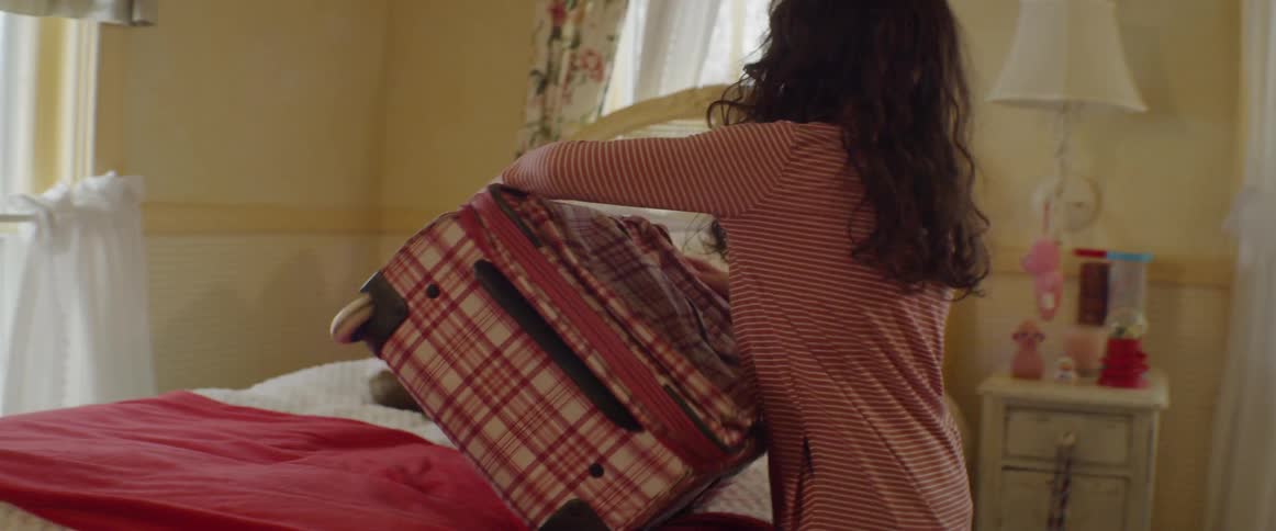 Child puts suitcase on a bed and unzips it