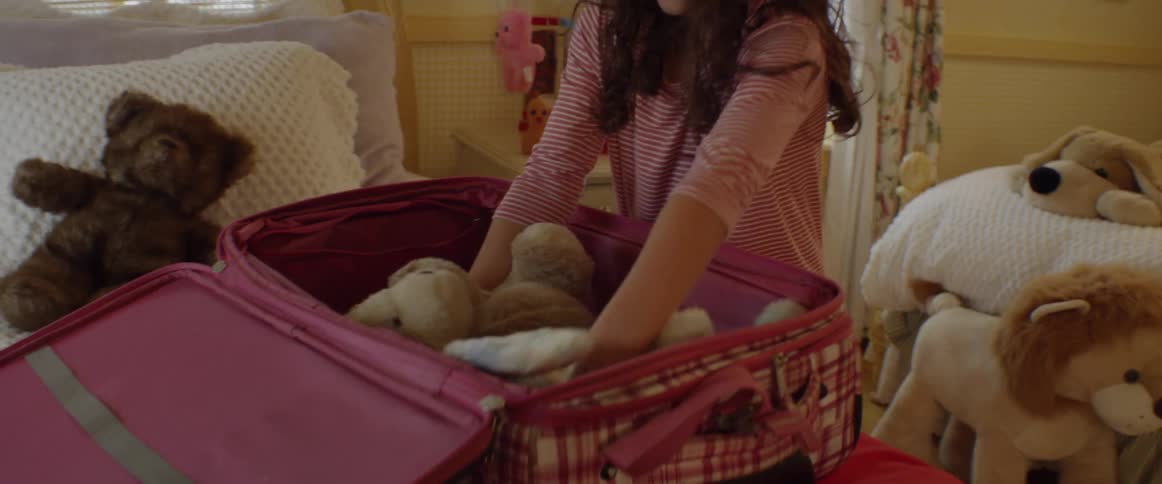 A young girl packs stuffed animals into a suitcase