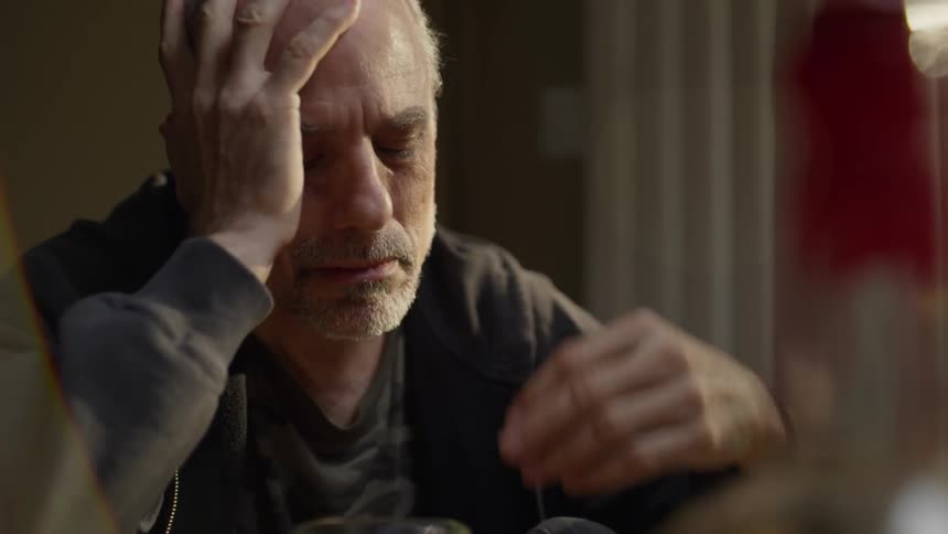 Man rests his head in his hands while drinking whiskey