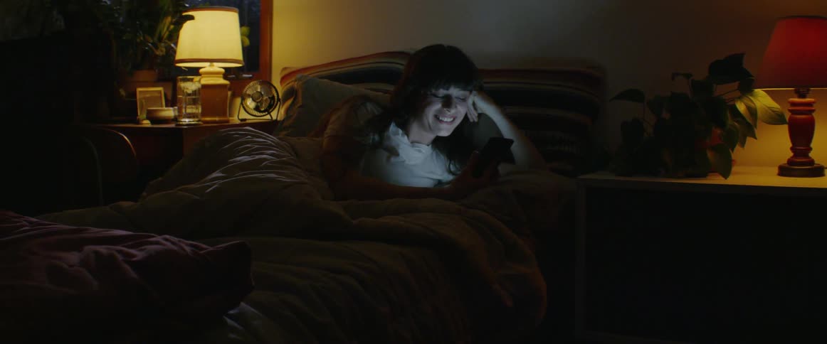 A woman is talking on her cell phone as she lies in bed at night