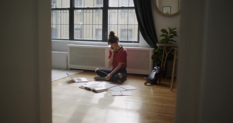 The woman is sitting on the floor in the room talking on the phone