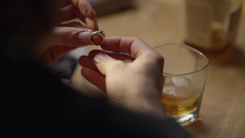 Man holds wedding rings while drinking whiskey