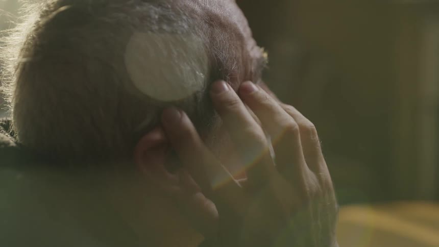 Sad man sitting at a table holding his head in a room