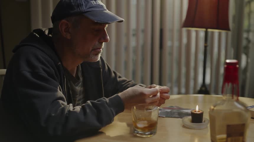 A man at a table with a candle and glass looking at something he's holding