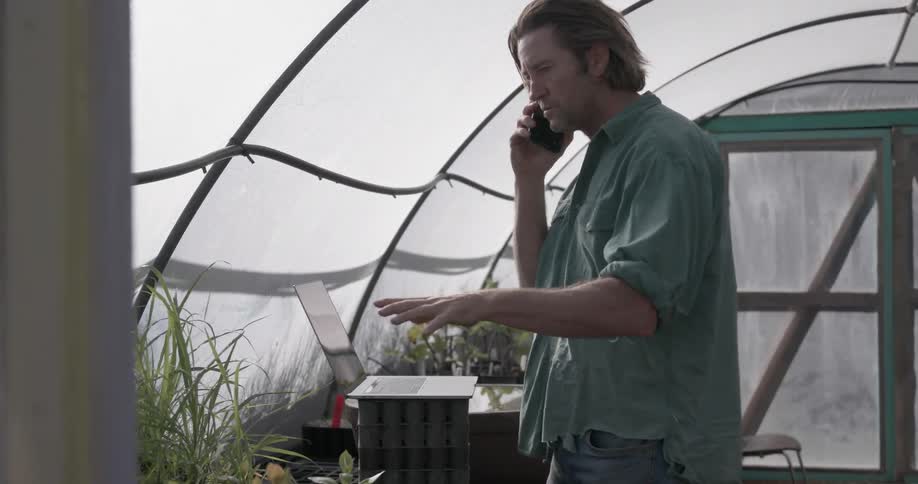 A man talks on the phone in his greenhouse