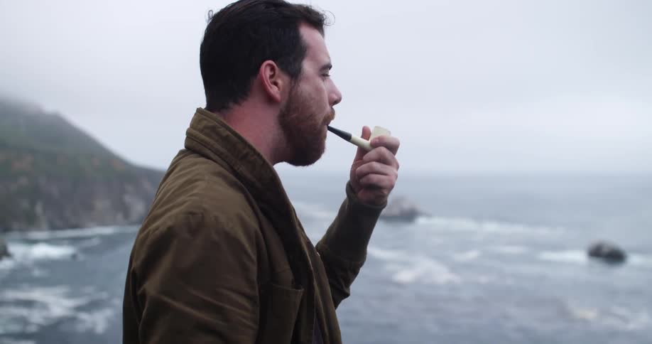 Man smoking a pipe as he looks over an ocean