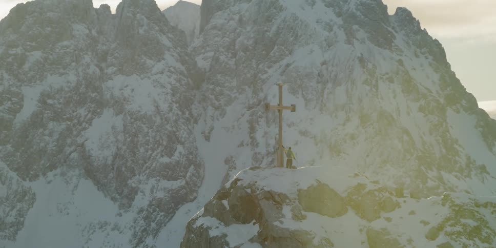 A man is standing near a giant cross on the mountain
