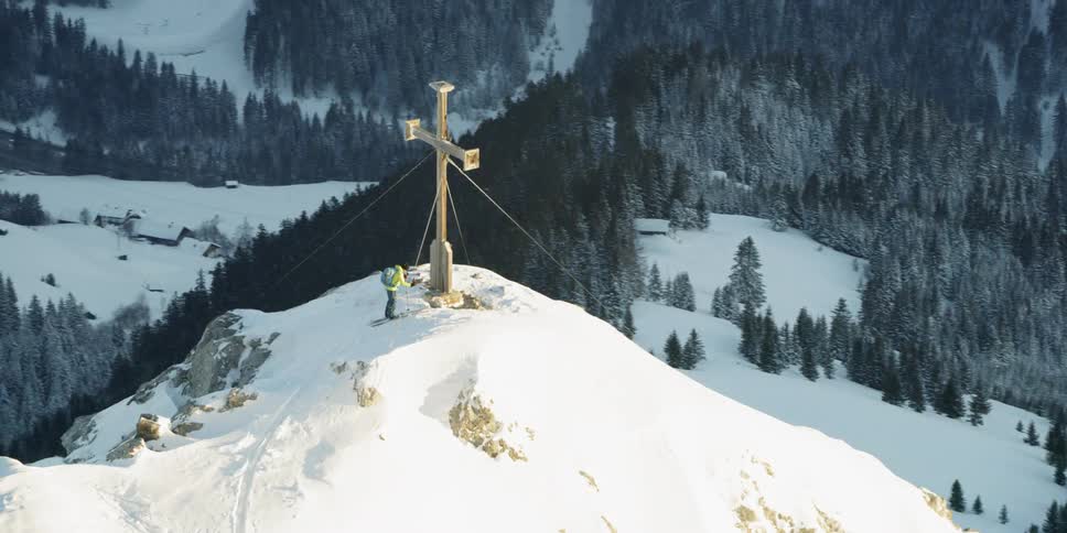 A skier stands on the peak near a cross