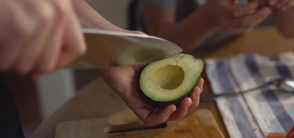 A man uses a knife to slice an avocado half