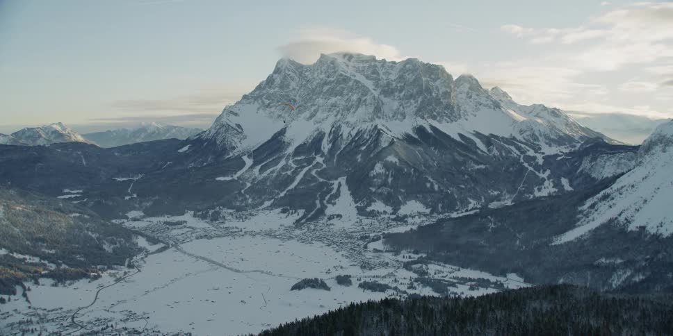 Person parasailing over snowy mountains