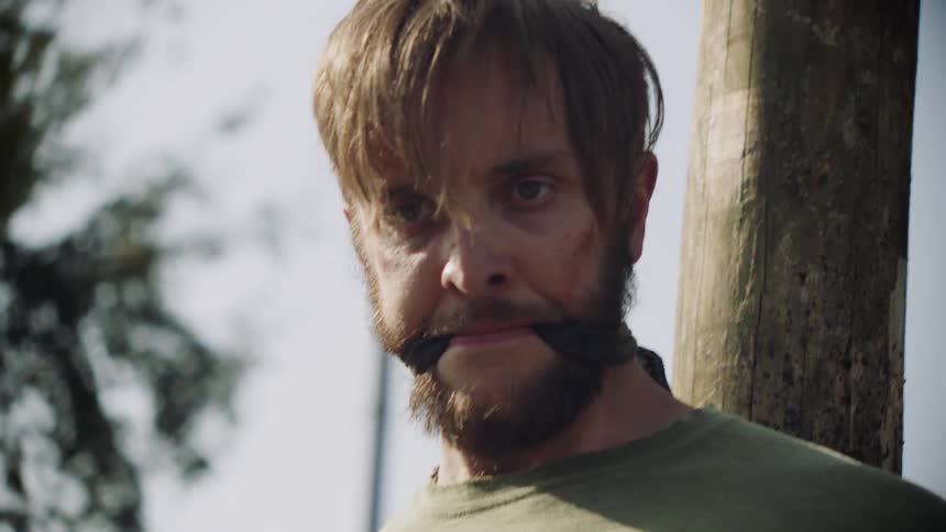 A gagged man is tied to a wood post