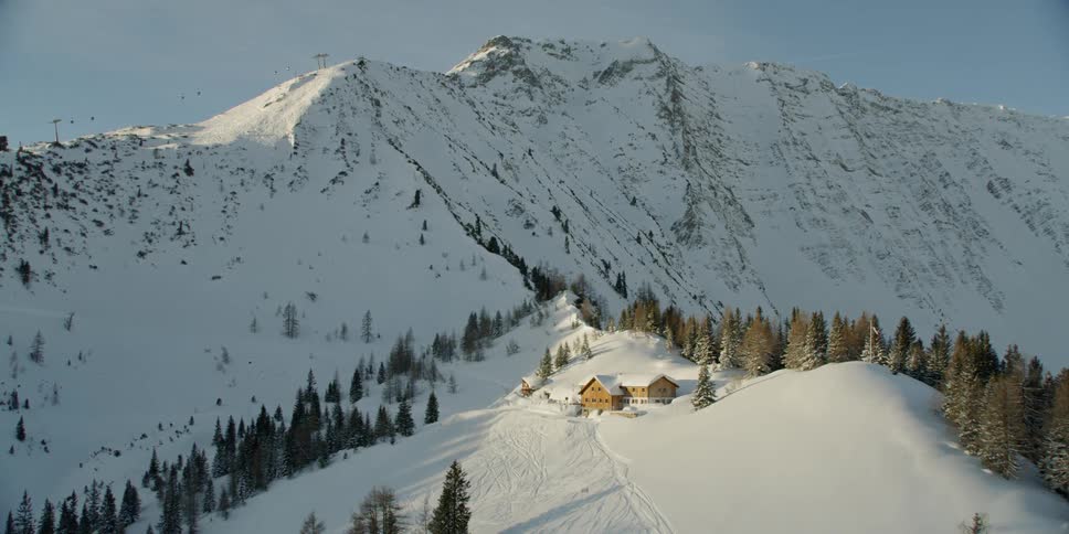 Sun shines down over snowy mountains with a building nestled on top