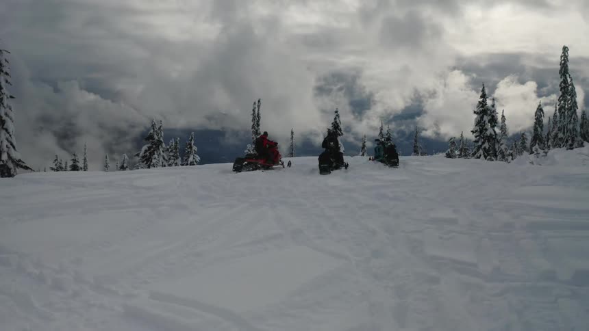 Three people on snowmobiles are parked on a hill