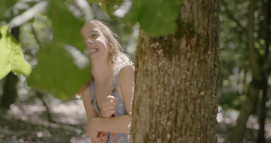 Little girl peeks out from behind tree and smiles