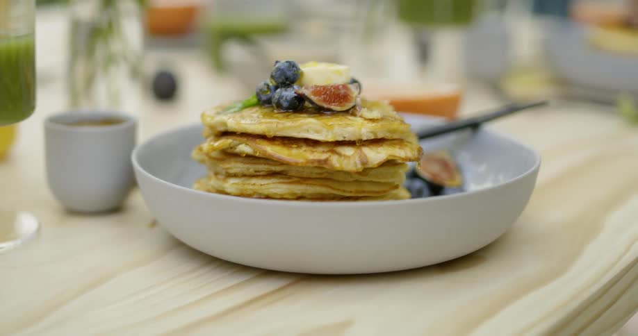 Person walks past a stack of blueberry pancakes on a plate on a table