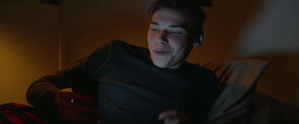 A man is talking on his cell phone as he lies in bed at night