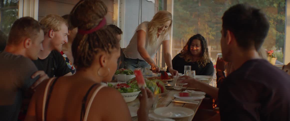 A woman cuts up pizza for a group of people
