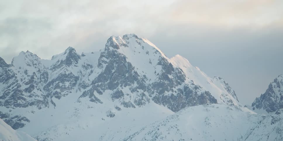 Snow covered mountains sit under a cloudy sky