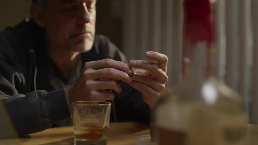 A man sitting at a table looks at wedding rings he is holding