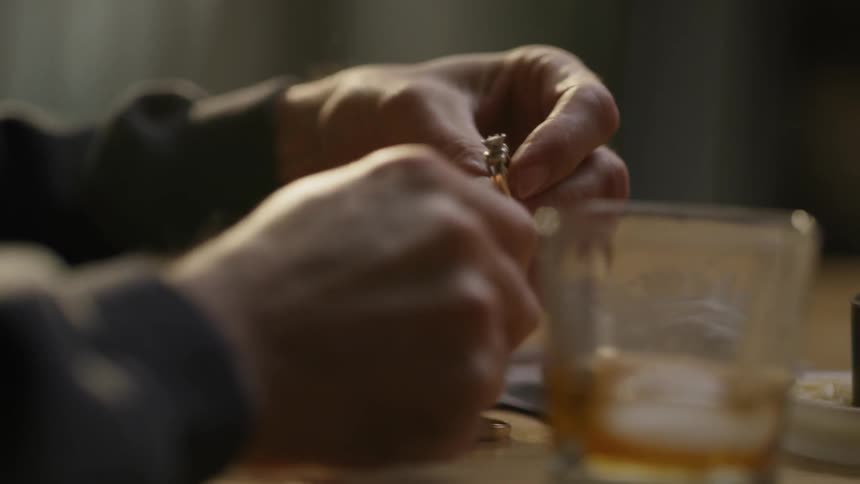 Man holds wedding rings while drinking whiskey