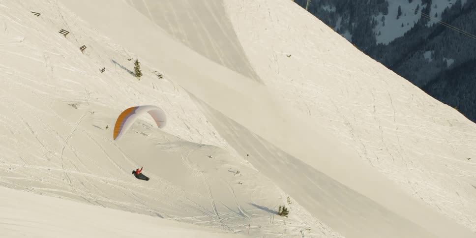 A person parasails down the snow covered hill