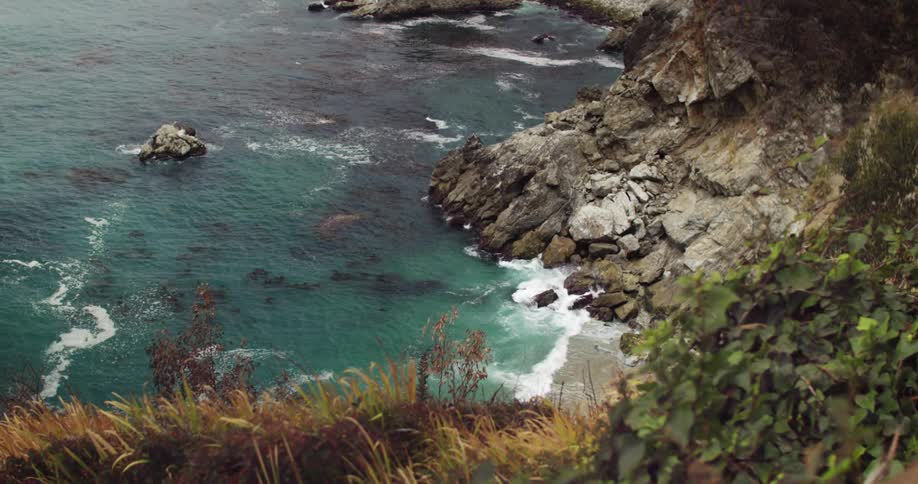 Waves crashing against the base of a cliff in big sur