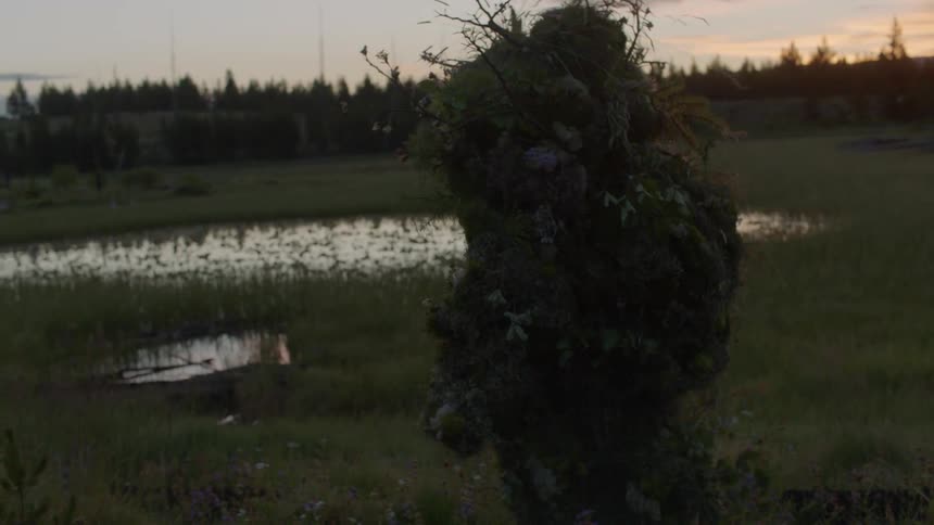 A person in a ghillie suit walks through the grass