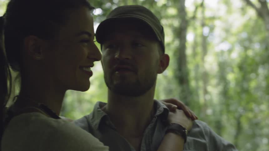 A man and woman hug as the man points towards the forest
