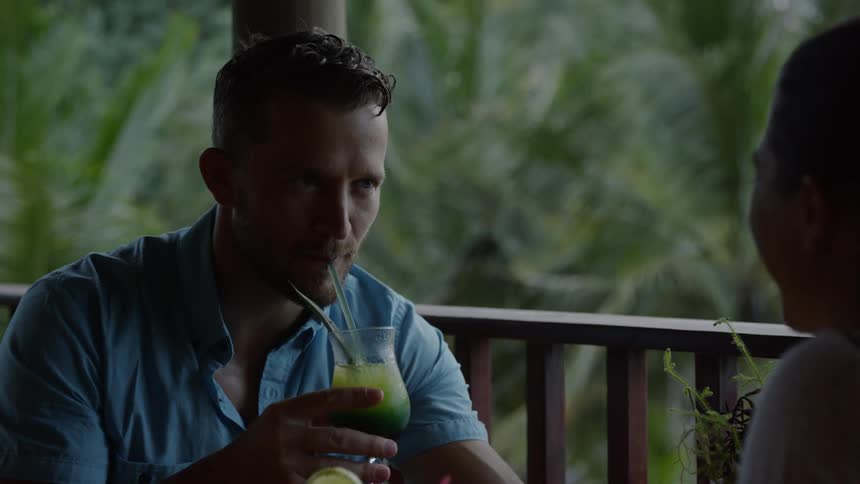 Man smiles as he drinks a green tropical drink