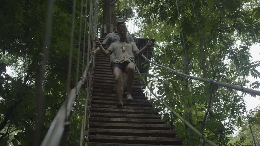 A man and woman walk down a bridge from a tree deck in the woods