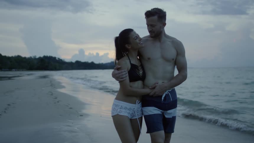 A couple walk on the beach while hugging