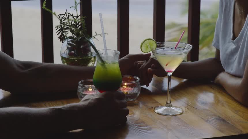 Two people hold hands as they sit down for drinks