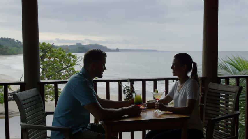 Man and woman drink cocktails on a beach patio