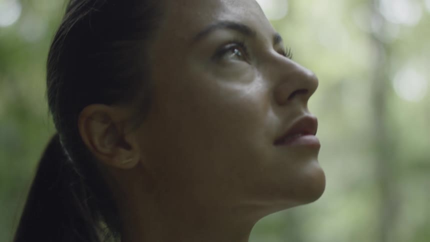 A woman stares upwards while outside in the woods