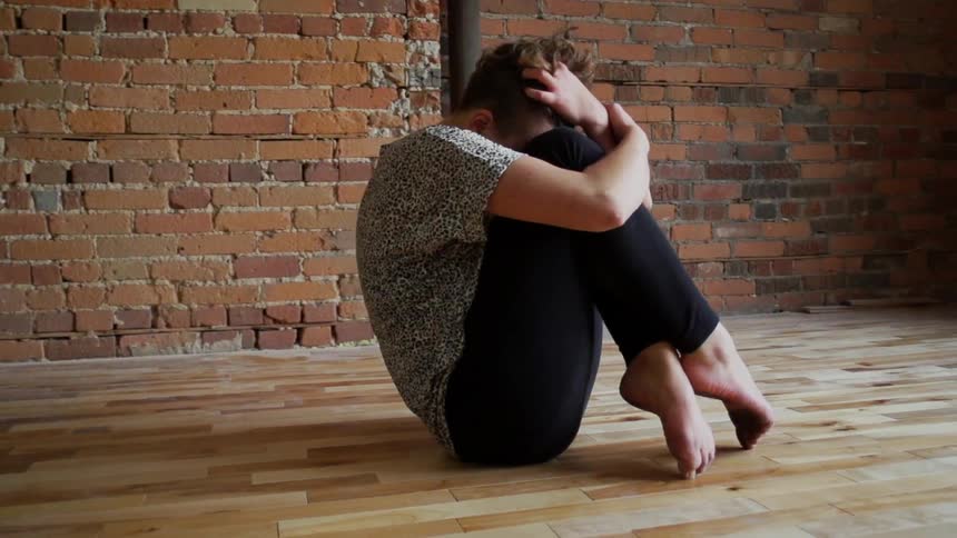Person sitting on a wood floor by a brick wall