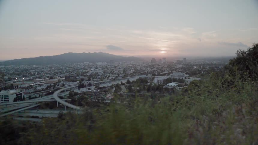 The sun is setting beyond a freeway running through a valley community