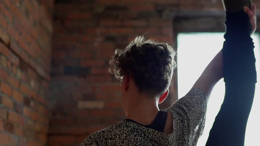 A woman stretching her leg over her head as she balances against a brick wall