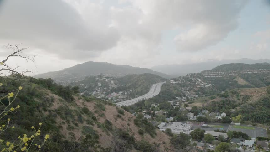 Traffic is flowing on a freeway through a valley during a cloudy day